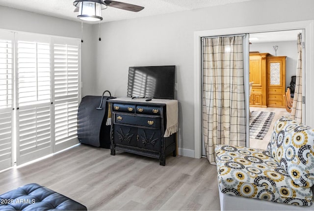 living area featuring baseboards, a ceiling fan, and wood finished floors