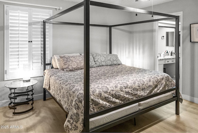 bedroom with baseboards, ensuite bath, and wood finished floors