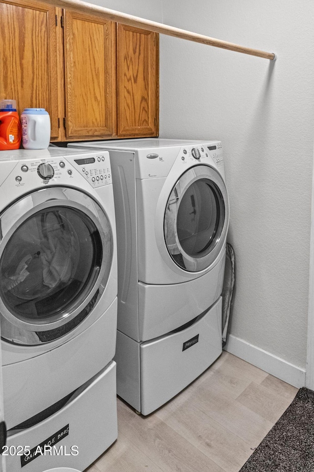 washroom featuring cabinet space, baseboards, and washer and clothes dryer