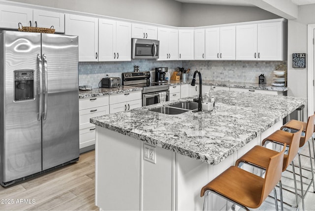 kitchen featuring white cabinetry, tasteful backsplash, a sink, light wood finished floors, and appliances with stainless steel finishes