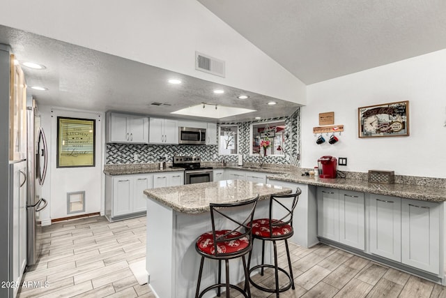 4013 E Delta Cir, Mesa, AZ 85206 - kitchen with appliances with stainless steel finishes, wood tiled floors, light stone countertops, a textured ceiling, and a breakfast bar area