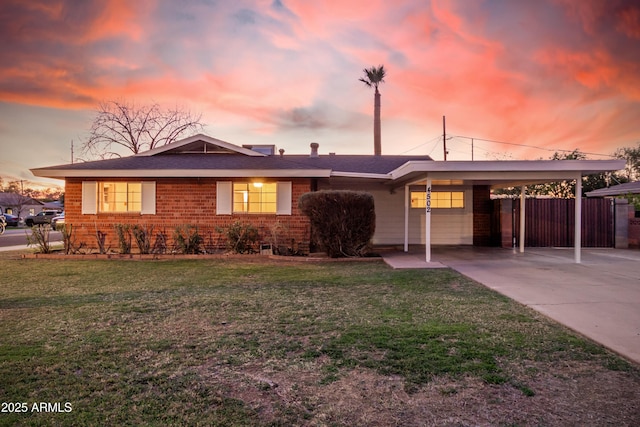 view of front of house with brick siding, concrete driveway, fence, a carport, and a front lawn