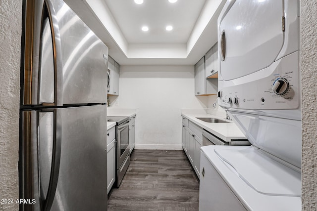 kitchen featuring white cabinets, a raised ceiling, appliances with stainless steel finishes, stacked washing maching and dryer, and dark hardwood / wood-style floors