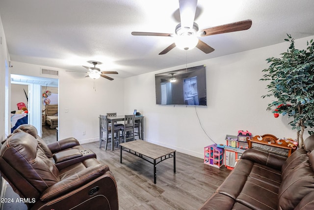 living area featuring a ceiling fan, a textured ceiling, baseboards, visible vents, and wood finished floors