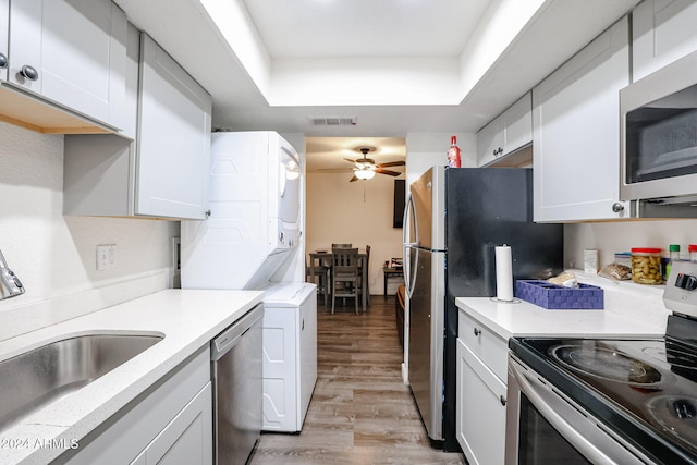 kitchen with appliances with stainless steel finishes, stacked washer / dryer, a tray ceiling, white cabinetry, and light hardwood / wood-style flooring