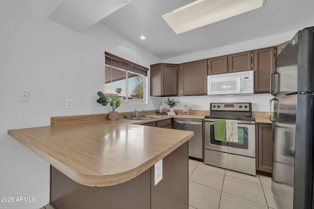 kitchen featuring light tile patterned flooring, dark brown cabinetry, a sink, stainless steel appliances, and a peninsula