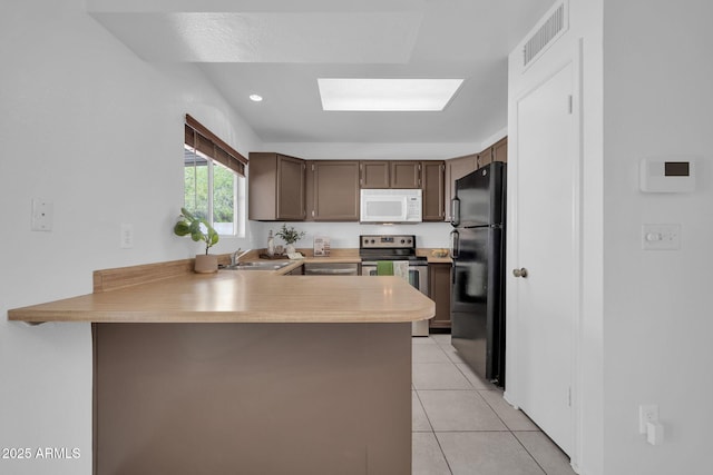 kitchen with electric range, visible vents, a sink, white microwave, and freestanding refrigerator