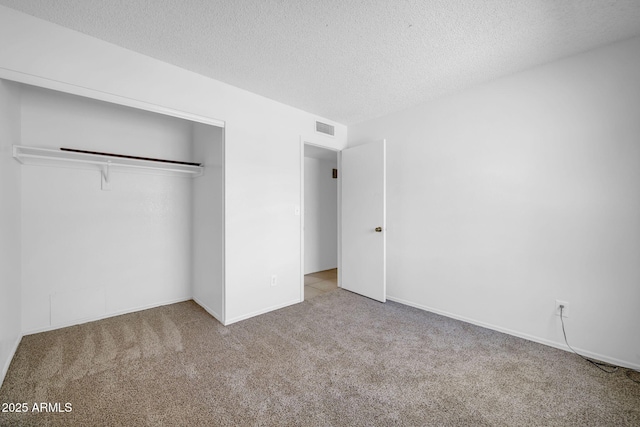unfurnished bedroom with a textured ceiling, carpet, baseboards, visible vents, and a closet