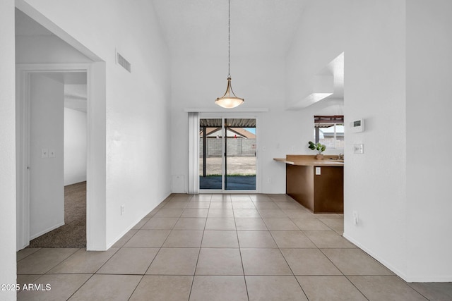 unfurnished dining area featuring high vaulted ceiling, light tile patterned flooring, and visible vents