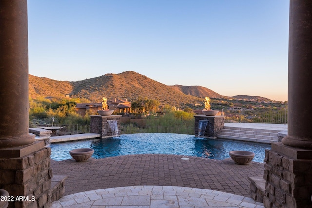 pool at dusk featuring a mountain view and pool water feature