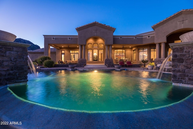 pool at dusk with pool water feature and ceiling fan