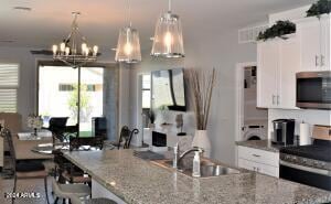 kitchen with sink, an inviting chandelier, light stone counters, white cabinets, and appliances with stainless steel finishes