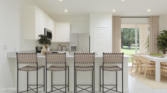 kitchen featuring stainless steel microwave, light countertops, a peninsula, a kitchen breakfast bar, and white fridge with ice dispenser