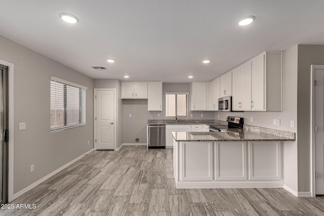 kitchen with kitchen peninsula, white cabinetry, dark stone counters, appliances with stainless steel finishes, and sink