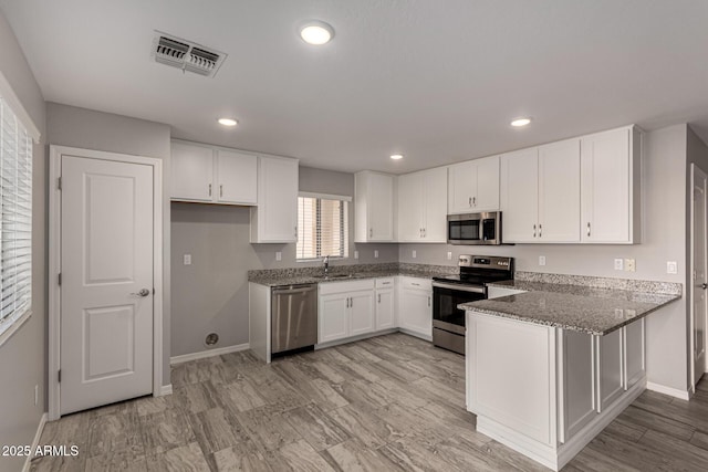 kitchen with kitchen peninsula, stainless steel appliances, white cabinets, dark stone countertops, and sink