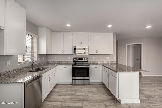 kitchen with kitchen peninsula, stainless steel appliances, white cabinetry, stone counters, and sink