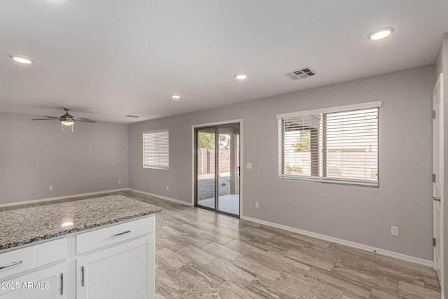 kitchen with light stone countertops, ceiling fan, and white cabinetry