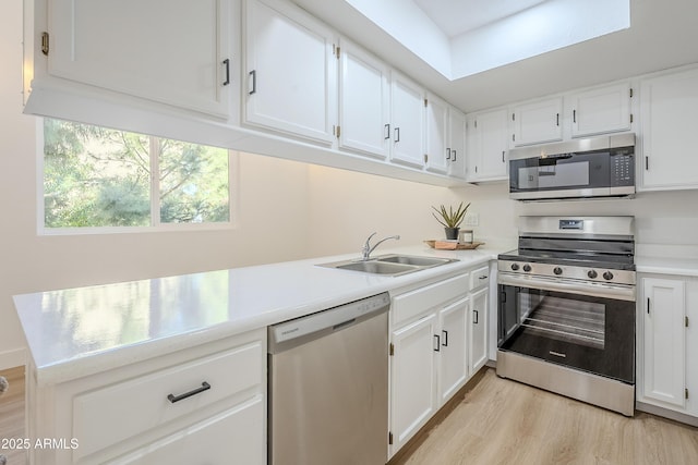 kitchen featuring kitchen peninsula, stainless steel appliances, sink, light hardwood / wood-style flooring, and white cabinets