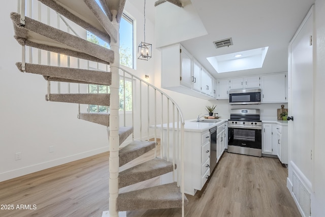 kitchen featuring an inviting chandelier, appliances with stainless steel finishes, decorative light fixtures, white cabinets, and light wood-type flooring