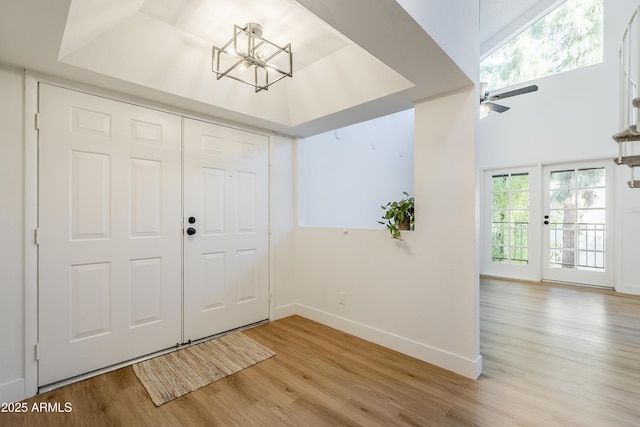 foyer featuring a tray ceiling, ceiling fan with notable chandelier, and light wood-type flooring