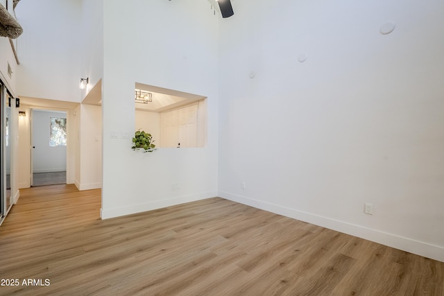 empty room featuring ceiling fan, light hardwood / wood-style floors, and a high ceiling