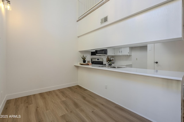 kitchen with a high ceiling, kitchen peninsula, light hardwood / wood-style floors, stainless steel electric stove, and white cabinets