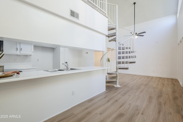 kitchen with white cabinetry, sink, a high ceiling, light hardwood / wood-style flooring, and kitchen peninsula