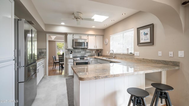 kitchen with sink, a breakfast bar, white cabinetry, stainless steel appliances, and kitchen peninsula