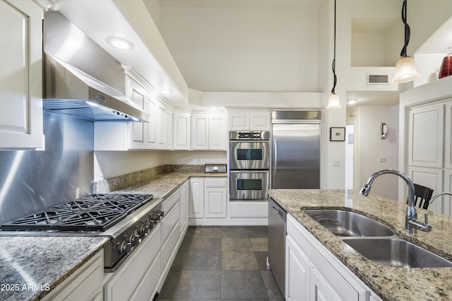 kitchen featuring sink, decorative light fixtures, white cabinets, stainless steel appliances, and wall chimney range hood