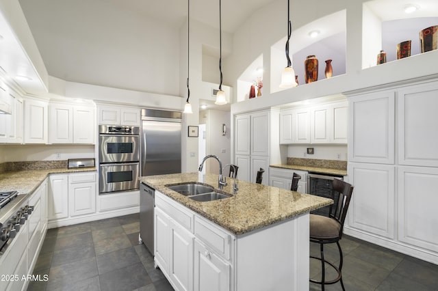 kitchen featuring sink, appliances with stainless steel finishes, pendant lighting, a kitchen island with sink, and white cabinets