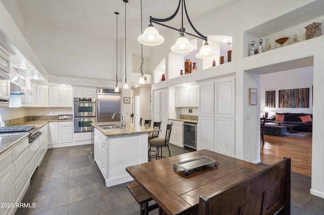 kitchen featuring sink, decorative light fixtures, appliances with stainless steel finishes, beverage cooler, and a kitchen island with sink