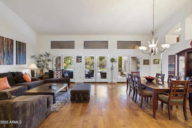 living room featuring a high ceiling, a notable chandelier, light hardwood / wood-style floors, and french doors