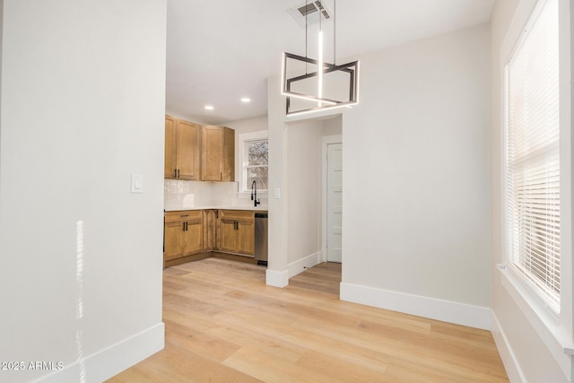 kitchen featuring sink, light hardwood / wood-style flooring, dishwasher, tasteful backsplash, and decorative light fixtures