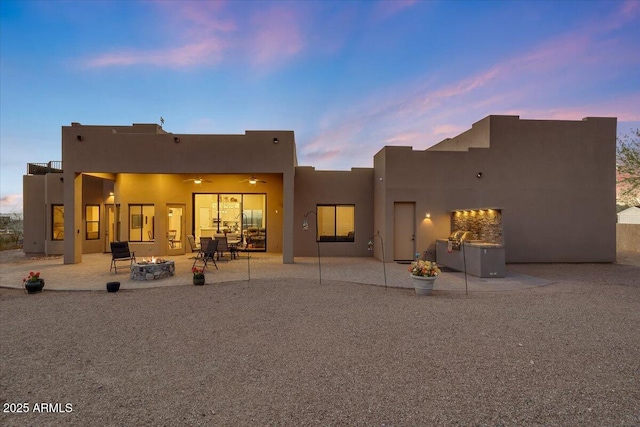 back house at dusk with a fire pit, ceiling fan, and a patio area