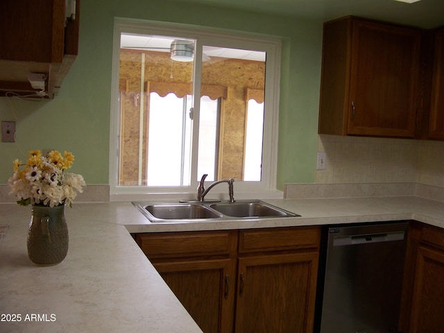 kitchen featuring brown cabinets, a sink, stainless steel dishwasher, light countertops, and decorative backsplash