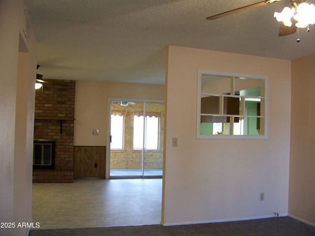 unfurnished room with ceiling fan, a brick fireplace, wainscoting, and a textured ceiling