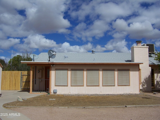 rear view of house with cooling unit, a chimney, and fence