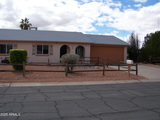 view of front facade featuring a fenced front yard, concrete driveway, roof with shingles, stucco siding, and a garage