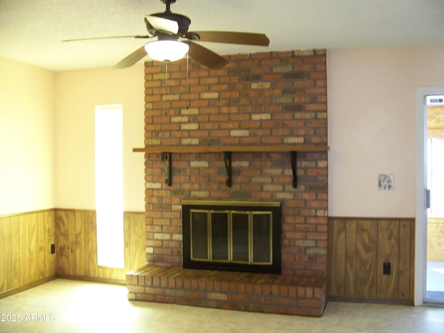 unfurnished living room featuring a brick fireplace, a healthy amount of sunlight, wood walls, and wainscoting