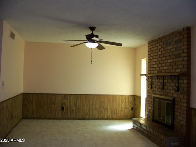 unfurnished living room with wooden walls, wainscoting, a brick fireplace, and visible vents