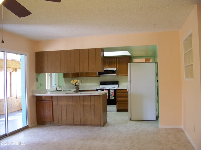 kitchen featuring a sink, stainless steel microwave, electric range oven, freestanding refrigerator, and a peninsula