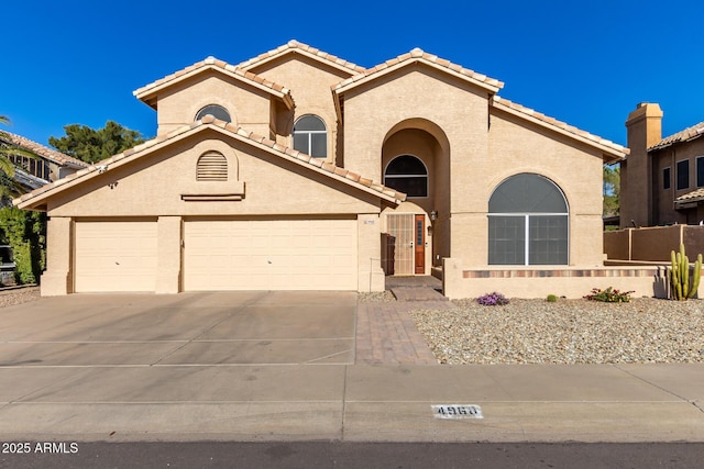 mediterranean / spanish house featuring a tiled roof, fence, concrete driveway, and stucco siding