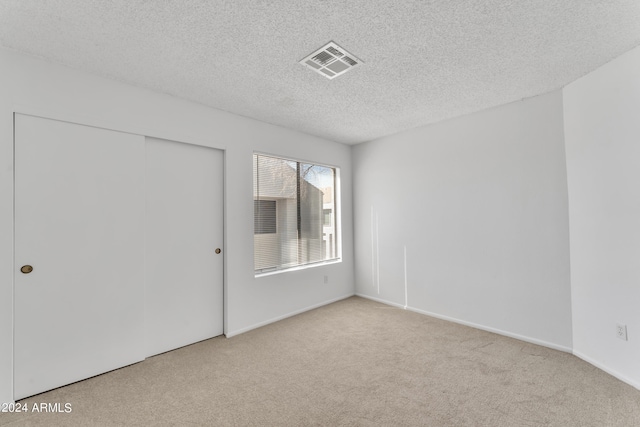 unfurnished bedroom with a closet, a textured ceiling, and light colored carpet