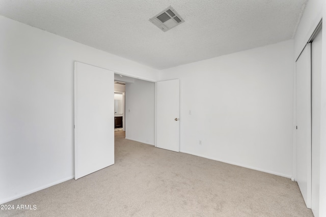 unfurnished bedroom featuring a closet, light carpet, and a textured ceiling