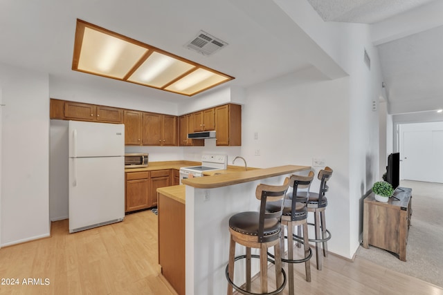 kitchen featuring a breakfast bar, light hardwood / wood-style floors, kitchen peninsula, and white appliances