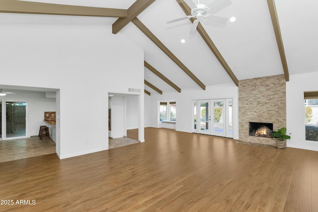 unfurnished living room featuring french doors, a stone fireplace, high vaulted ceiling, hardwood / wood-style flooring, and ceiling fan