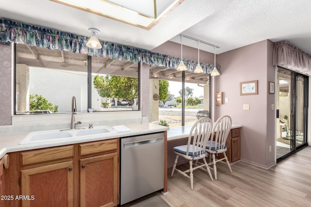 kitchen featuring sink, decorative light fixtures, a textured ceiling, light hardwood / wood-style flooring, and stainless steel dishwasher