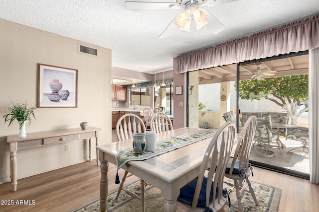 dining space with hardwood / wood-style flooring, ceiling fan, sink, and a textured ceiling