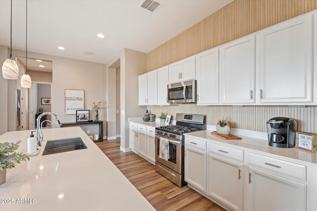 kitchen featuring a sink, stainless steel appliances, light countertops, white cabinetry, and light wood-type flooring