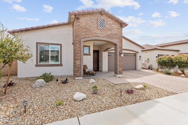 mediterranean / spanish-style house with stucco siding, driveway, a tile roof, stone siding, and an attached garage